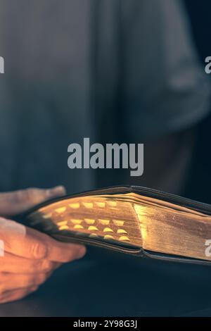 Ein Mann hält eine Bibel in den Händen. Bibel mit goldenen Seiten. Religionskonzept. Stockfoto
