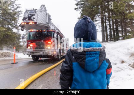 Boy beobachtet Feuerwehrleute in Aktion während eines verschneiten Winternotfalls und stellt Sicherheit, Heldentum und Gemeindedienst zur Schau. Selektiver Fokus Stockfoto