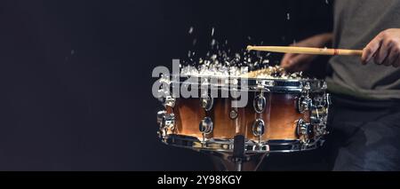 Trommel klebt auf Snare-Trommel mit Spritzwasser auf schwarzem Hintergrund. Stockfoto