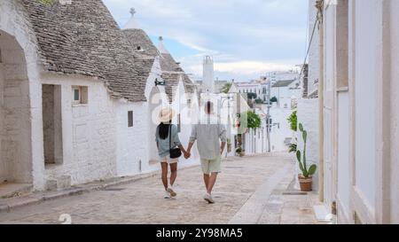 Ein Paar spaziert Hand in Hand entlang einer engen Kopfsteinpflasterstraße, die von weiß getünchten Trullihäusern gesäumt ist, und taucht in die Schönheit von Alberobello Apulias Uniq ein Stockfoto