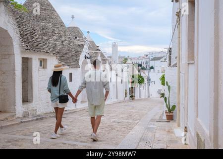 Ein paar Spaziergänge Hand in Hand entlang der malerischen Straßen von Alberobello Apulien, umgeben von berühmten Trullihäusern. Die Sonne leuchtet sanft auf Stockfoto