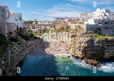 Polignano a Mare eingebettet in die atemberaubenden Klippen von Apulien, genießen die Menschen die Sonne an einem ruhigen Strand, während azurblaue Wellen sanft über die Küste schlängeln und so einen herrlichen Ausblick auf die Sonne schaffen Stockfoto