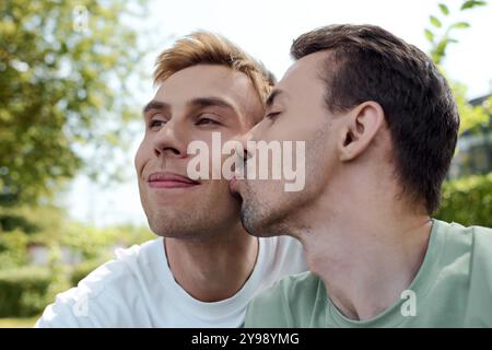 Ein fröhliches Paar teilt sich einen liebevollen Kuss, während es einen warmen Nachmittag in einem lebhaften Park genießt. Stockfoto