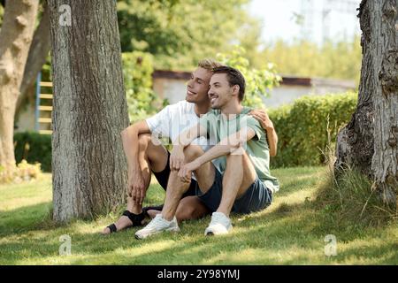 Ein gutaussehendes schwules Paar entspannt sich auf dem Gras, teilt Lachen und genießt die Gesellschaft. Stockfoto