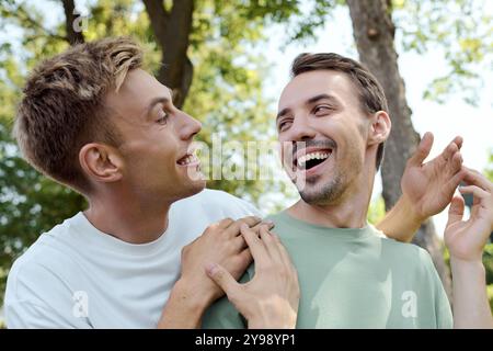 Zwei lächelnde Männer teilen sich einen unbeschwerten Moment, umgeben von Natur und Sonnenlicht. Stockfoto