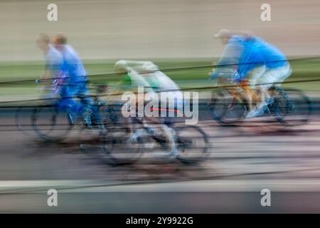 Schwenkfoto, das die dynamische Bewegung von Radfahrern bei Nacht durch die Straßen der Stadt fängt und eine lebendige Unschärfe aus Farben und Bewegungen erzeugt. Stockfoto