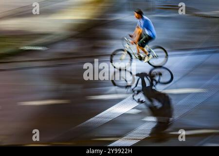 Dynamische Schwenkaufnahme, bei der ein Radfahrer in Bewegung auf einer nassen Stadtstraße bei Nacht aufgenommen wird, wobei Geschwindigkeit und Bewegung betont werden. Stockfoto