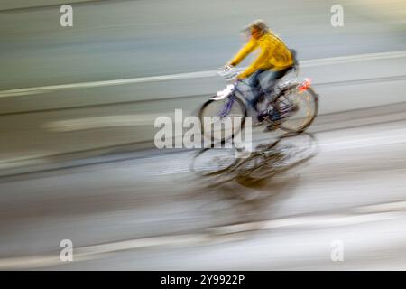 Ein dynamisches Schwenkbild, das einen Radfahrer in Bewegung durch die Straßen der Stadt bei Nacht erfasst und dabei Bewegung und urbanes Leben hervorhebt. Stockfoto