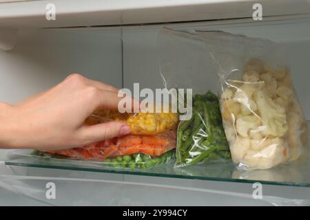 Eine Frau, die Plastiktüte mit gefrorenem Mais aus dem Kühlschrank nimmt Stockfoto