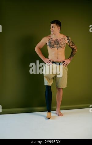 Ein junger Mann mit lebendigen Tattoos zeigt seine Beinprothese, während er in einem Studio voller Kreativität posiert. Stockfoto