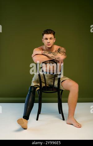 Ein junger Mann mit komplizierten Tattoos und einer Beinprothese zeigt seine Stärke in einem kreativen Studio-Raum. Stockfoto