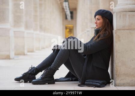 Stilvolle schöne Frau in Beret und Stiefeln, die sich im Pariser Courtyard France entspannen Stockfoto