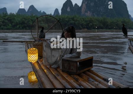 Hanfu Girl hält eine beleuchtete Laterne auf einem Bambusfloß mit Kormoranvögeln in der Nacht Stockfoto