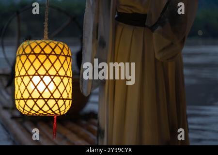 Hanfu Mädchen hält nachts eine beleuchtete Laterne auf einem Bambusfloß Stockfoto