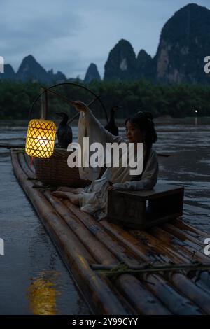 Hanfu-Mädchen, das eine Laterne auf einem Bambusfloß hält, Xingping, China. Vertikal Stockfoto