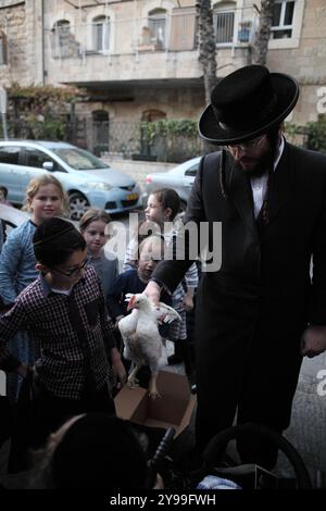 Ultra Orthodox man zeigt Kindern und Kleinkindern einen Hahn, der ihn ansieht und anfasst, bevor er für Kapprot getötet wird, kurz vor Yom Kippur oder dem Tag der Sühne. Stockfoto