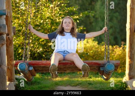 Glückliches Mädchen auf einer Schaukel. Kind auf dem Spielplatz, schwingend auf einer großen Holzwippe. Sommeraktivitäten im Freien für Kinder Stockfoto