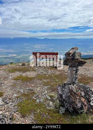 Holzbank und Inukshuk mit Panoramablick auf das Smithers Valley vom Hudson Bay Mountain, British Columbia, Kanada, unter bewölktem, weitläufigem Himmel Stockfoto