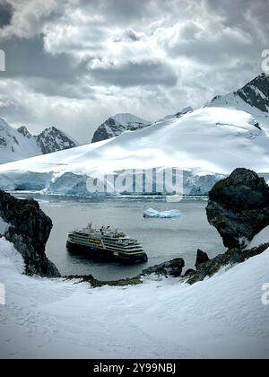 Das National Geographic Endurance Kreuzfahrtschiff liegt in einer atemberaubenden antarktischen Bucht, umgeben von schneebedeckten Gipfeln und dramatischen Eisformationen Stockfoto