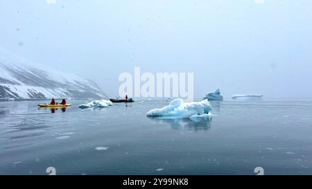 Passagiere vom Nat Geo Endurance Kajak fahren an schwimmenden Eisbergen und ruhigen Gewässern in der Nähe der Trinity Peninsula in der Antarktis, umgeben von schneebedeckten Gipfeln Stockfoto