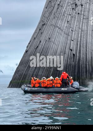 Touristen in orangefarbenen Jacken erkunden die gewaltigen geologischen Formationen des Edinburgh Rock, der sich auf den abgelegenen South Shetland Islands in der Antarktis befindet Stockfoto