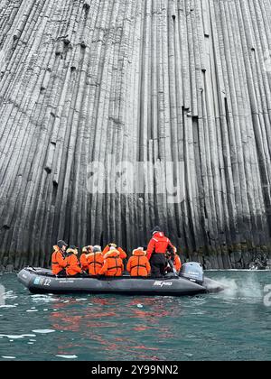 Touristen in orangefarbenen Jacken erkunden die gewaltigen geologischen Formationen des Edinburgh Rock, der sich auf den abgelegenen South Shetland Islands in der Antarktis befindet Stockfoto