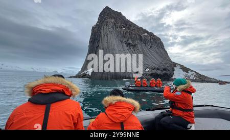 Touristen in orangefarbenen Jacken erkunden die gewaltigen geologischen Formationen des Edinburgh Rock, der sich auf den abgelegenen South Shetland Islands in der Antarktis befindet Stockfoto