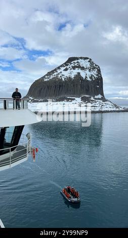 Passagiere an Bord der Lindblad Nat Geo Endurance beobachten ein kleines Expeditionsboot, das durch die ruhigen Gewässer in der Nähe des Edinburgh Rock in der Antarktis fährt Stockfoto