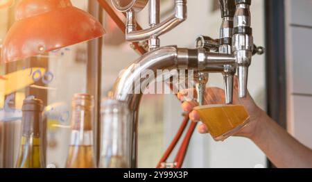 Vom Barkeeper aus dem Bierhahn im Pub wird kaltes Bier in ein Glas gegossen. Horizontales Bild eines Bierglases an der Bar. Stockfoto