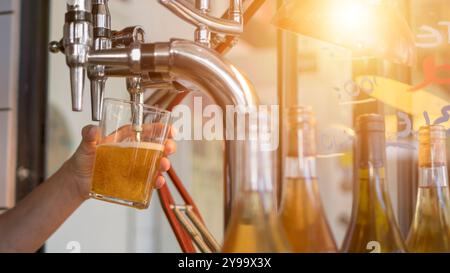 Vom Barkeeper aus dem Bierhahn im Pub wird kaltes Bier in ein Glas gegossen. Horizontales Bild eines Bierglases an der Bar. Stockfoto