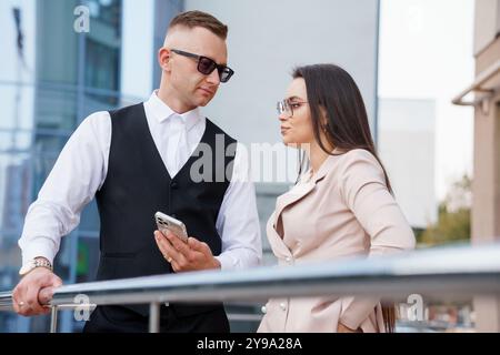 Stilvolles junges Paar, das sich mit Smartphone-Gesprächen in moderner urbaner Umgebung beschäftigt. Stockfoto