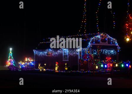 In einem Stadtpark im Nordosten von Ohio steht ein kleines, festlich dekoriertes Cottage mit Weihnachtslichtern und thematischen Figuren unter hohen Lichterketten. Stockfoto