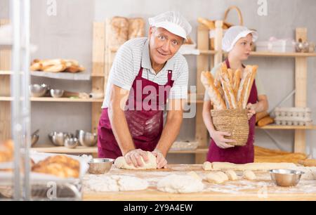 Senior Mann arbeitet in der Bäckerei als Bäcker, Knete Teig, arbeitet mit Mehl. Stockfoto