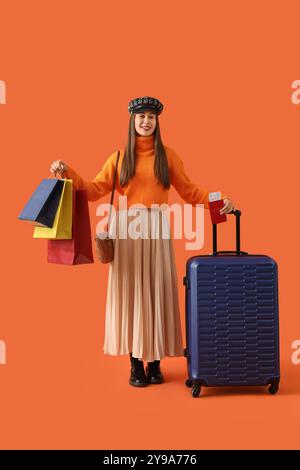 Weibliche Touristen in Herbstkleidung mit Taschen und Koffer auf orangefarbenem Hintergrund Stockfoto