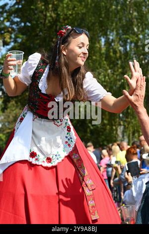 Badacsony, Balaton, Ungarn - 8. September 2024: Straßenparade des Weinerntefestes, junge Frau auf Stelzen mit rotem Kleid, die hohe fünf gibt Stockfoto