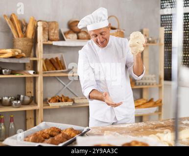 Senior Mann arbeitet in der Bäckerei als Bäcker, Knete Teig, arbeitet mit Mehl. Stockfoto
