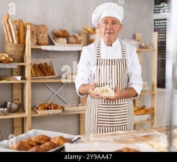 Senior Mann arbeitet in der Bäckerei als Bäcker, Knete Teig, arbeitet mit Mehl. Stockfoto