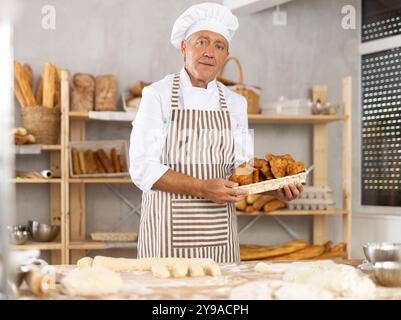 Erfolgreich gereifter Bäcker, der Croissants in der Bäckerei hält Stockfoto