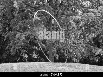 DeCordova Sculpture Park - Lincoln, Massachusetts - Ein metallischer Ring scheint über dem Boden zu schweben, der einen Baum im Hintergrund umgibt. Erfasst o Stockfoto