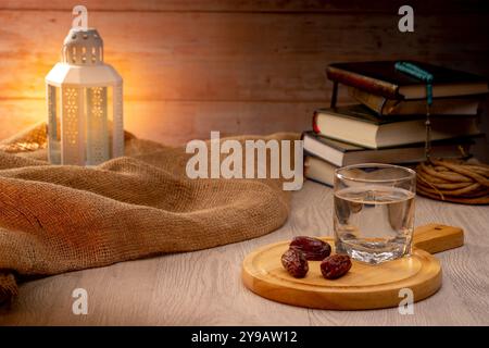 Viele Dattelpalmen stehen auf Schüsseln, Tellern, einer Tasse Wasser und Quran, eine Lampe im Islami-Stil auf den Holztischen, um auf die Zeit von Iftar zu warten, mit dem Co. Stockfoto