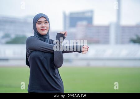 Eine junge asiatische muslimische Frau mit schwarzem Hijab tragt und läuft morgens in einem Freiluftstadion. Modernes muslimisches Frauenkonzept, muslimische W Stockfoto