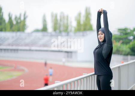 Eine junge asiatische muslimische Frau mit schwarzem Hijab tragt und läuft morgens in einem Freiluftstadion. Modernes muslimisches Frauenkonzept, muslimische W Stockfoto