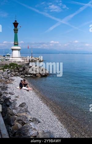 Mann, der am Ufer des Lemansees mit dem Leuchtturm im Hintergrund in Evian les Bains in den Alpen im Departement Haute-Savoie entspannt Stockfoto