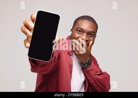 Überraschter afrikanischer junger Mann, der Smartphone zeigt und sich über den Erfolg freut, auf weißem Hintergrund. Stockfoto