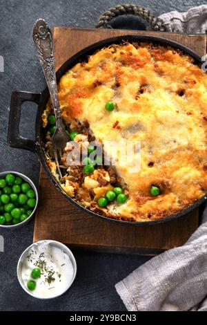 Shepherd's Pie mit Hackfleisch, Kartoffeln und Käse auf schwarzem Hintergrund, Blick von oben. Traditioneller hausgemachter Kartoffelauflauf mit grüner Erbse. Stockfoto