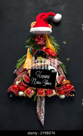 Weihnachtsbaum aus Käse- und Fleischvorspeisen auf dunklem Hintergrund. Winterferien-Snack. Draufsicht. Stockfoto