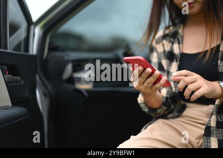 Zugeschnittene Aufnahme einer Touristenfrau, die ihr Handy benutzt, während sie mit geöffneter Tür im Auto sitzt Stockfoto