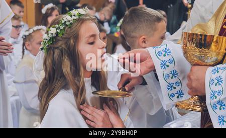 Lida, Weißrussland - 15. Juni 2021: Mädchen empfängt erste heilige Kommunion vom Priester in der Kirche Stockfoto