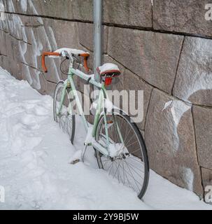 Stockholm, Schweden - 9. März 2023: Ein einsames grünes Fahrrad, das im verschneiten Stockholm an eine Straßenlaterne gekettet ist und auf seinen Besitzer wartet, wenn der Schnee schmilzt Stockfoto