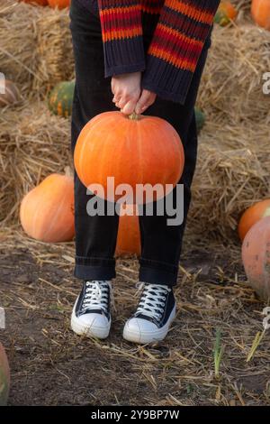 Eine Person, die einen großen orangefarbenen Kürbis am Stiel hält Stockfoto